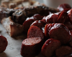 Summary graphic: A pile of sliced sausage links with a pork chop in the background.