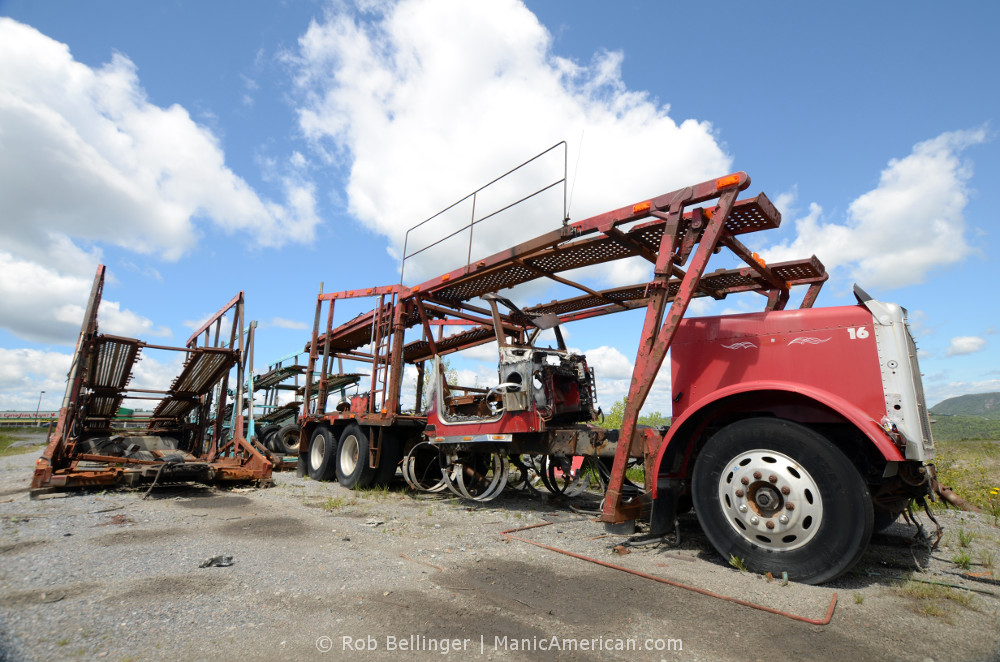 An abandoned car carrier truck, missing its cab, sits under a blue sky. Corner Brook, Newfoundland.