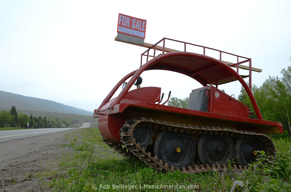 An old red snowmobile sits for sale on the side of a two-lane highway in southwest Newfoundland..