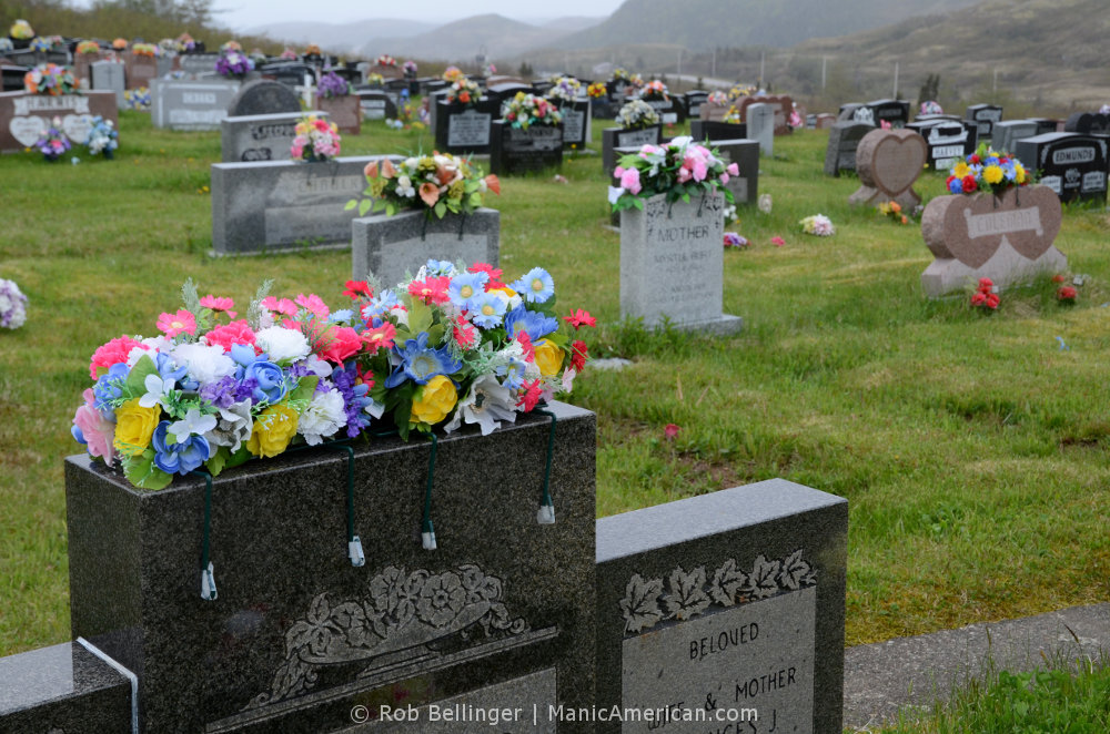Plastic flowers sit atop tombstones in the rain. Outside Isle aux Morts, Newfoundland.