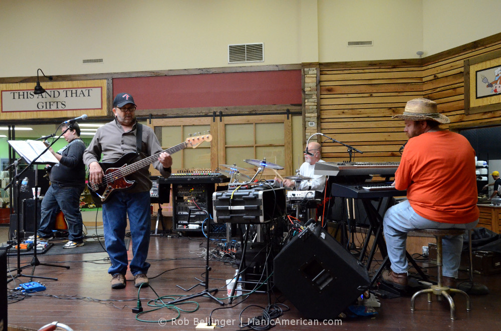 A band of four middle-aged musicians plays rock music in the dining area of a mall.