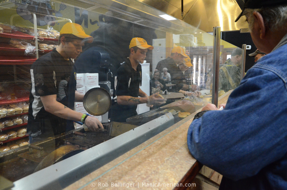 Customers wait for their burgers, while four employees cook them on the other side of a glass divider.