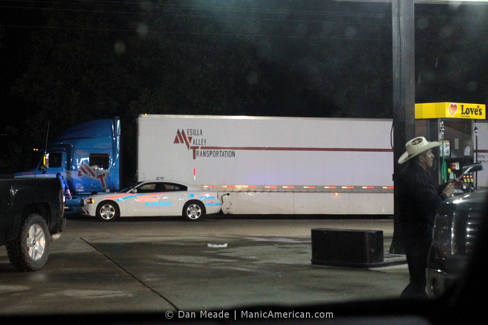 A cowboy wipes his windshield as a police officer approaches a big rig