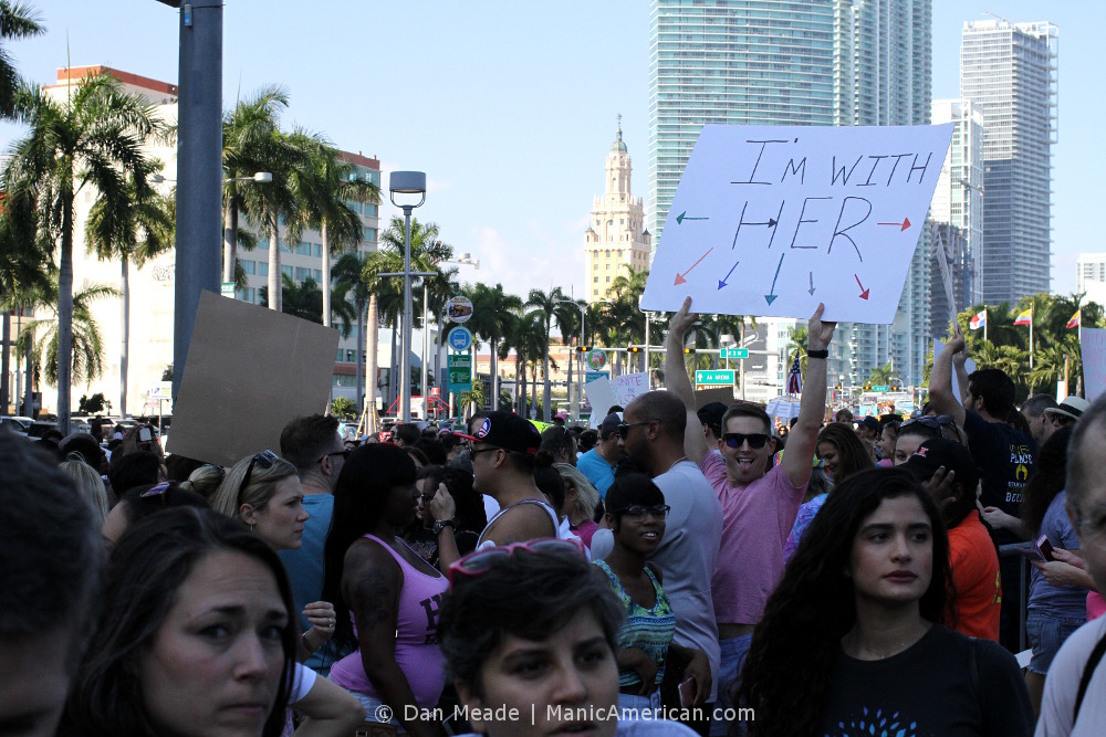 A man holds up an I'M WITH HER sign pointing all around