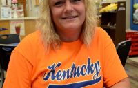 A woman in a shirt that says Kentucky sitting down at a table in a restaurant