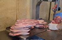 Making Kentucky barbecue: A band saw being used to slice frozen pork shoulder, with a pile of slices