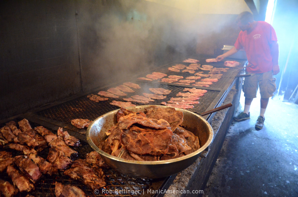 Making Kentucky barbecue: In the foreground, a bowl of cooked pork shoulder. In the background, a man putting raw pork shoulder on the grill.