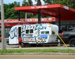 Summary graphic: A camping trailer used as a mobile food truck, hitched to a pickup truck which is stopped at a gas station along Lamar Avenue south of 240. The trailer is emblazoned with graffiti-style lettering reading “Kailynn's Lunch Box.”