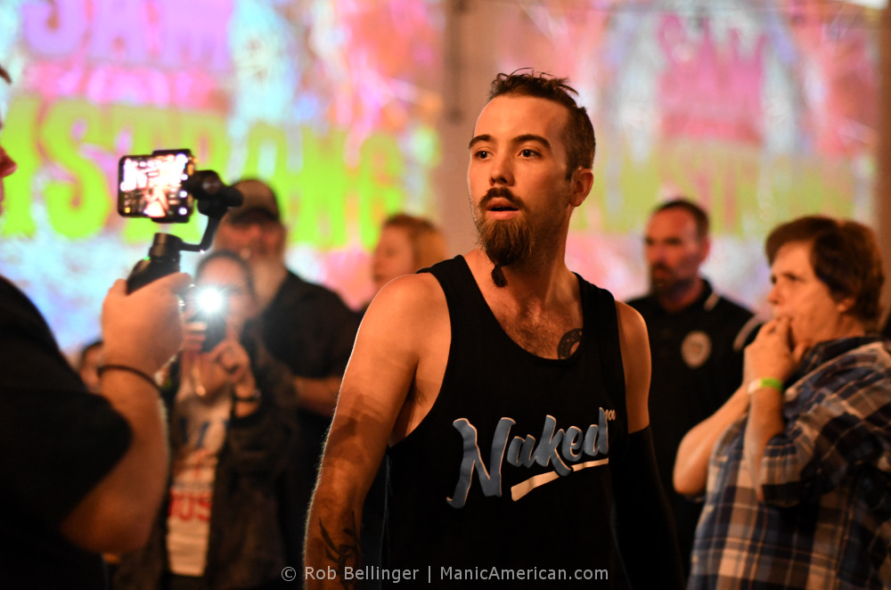 Surrounded by fans, Sam Armstrong approaches the ring wearing a shirt that says Naked