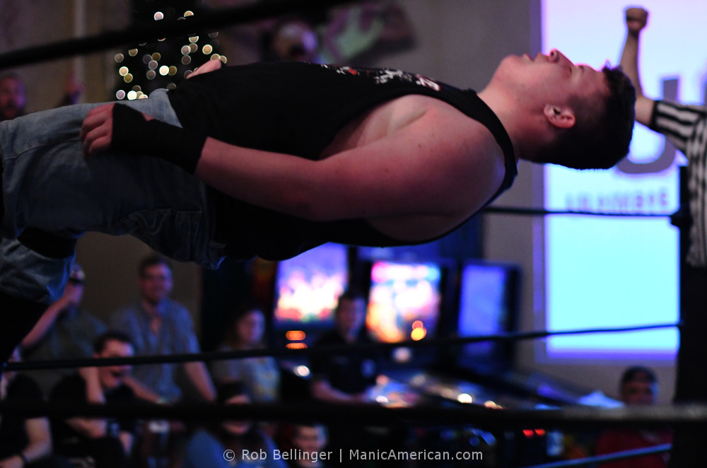Walker Hayes falls to the mat, seen between the ropes of the ring, parallel to the floor