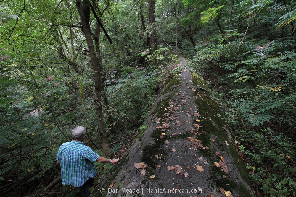 a man stands next to a stone aqueduct overgrown with moss