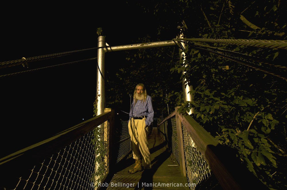 A bearded man standing on a pedestrian swing bridge at night