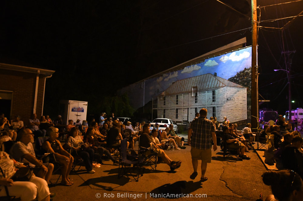 Dozens of people in lawn chairs sitting in front a building with a mural of an old hotel