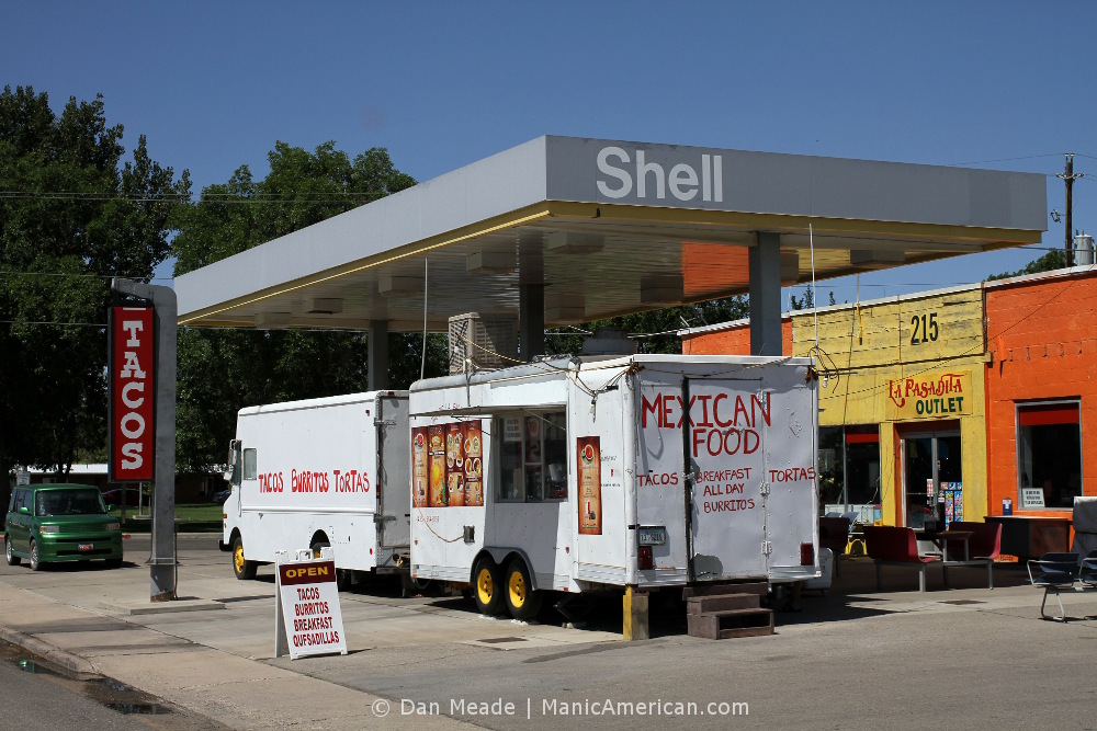 Two food trucks under a former gas station's awning.