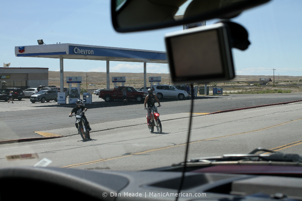 Two motorbikers pull out of a functioning gas station.