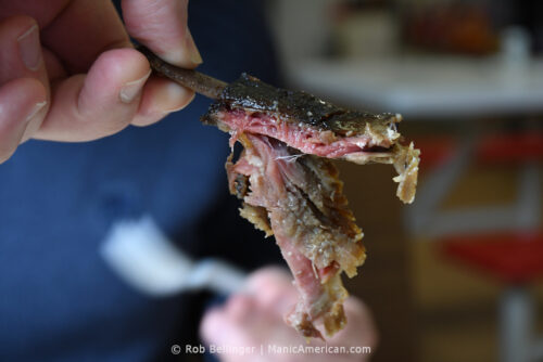 A hand holds up a smoked mutton rib. The meat is falling apart.
