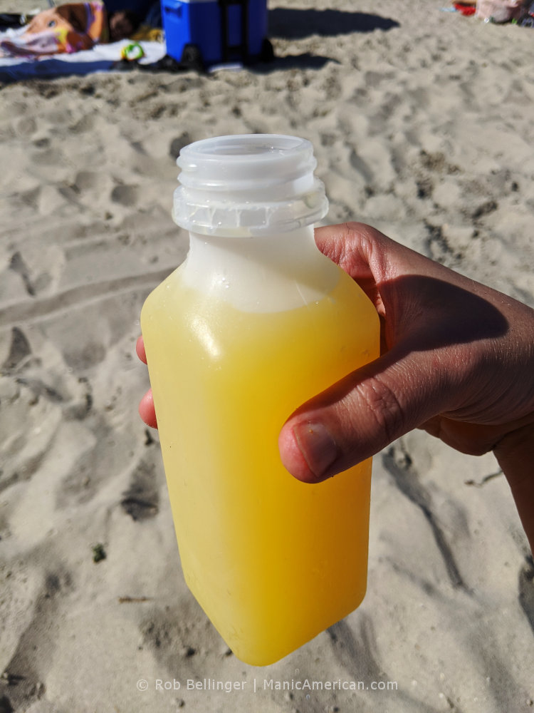 a plastic bottle containing a yellow alcoholic beverage, known as a nutcracker, on rockaway beach
