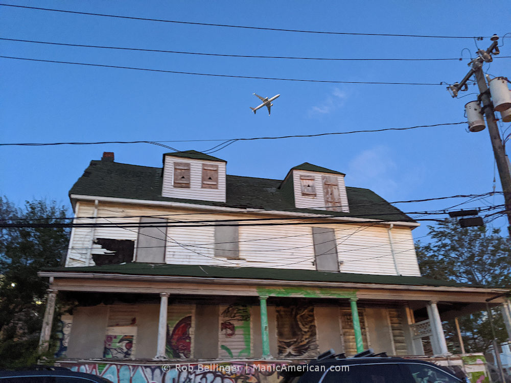 a plane takes off over an abandoned house covered in graffiti in rockaway beach