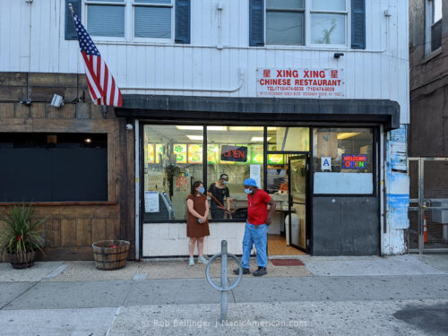 A man leaves a small Chinese-American restaurant on Rockaway Beach while a woman waits for her order and a worker mops the floor