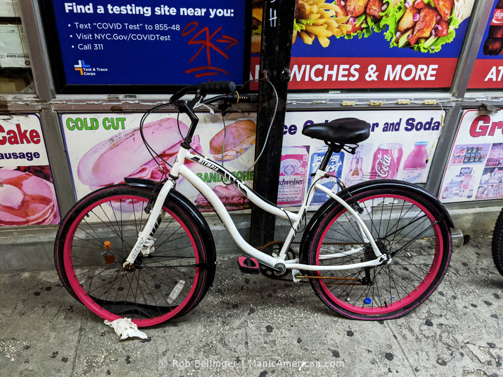 a beach crusier bike with two flat tires locked to the front of a deli in rockaway beach, with covid testing signs and graffiti