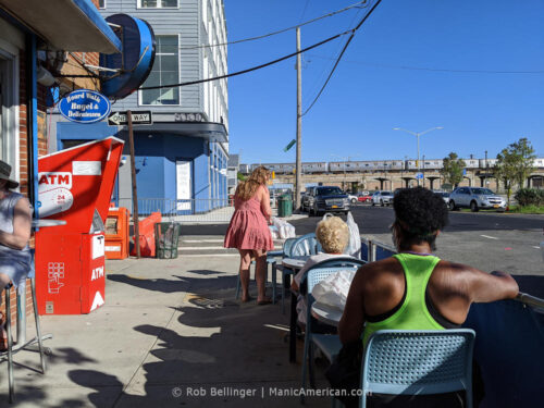 a sidewalk dining area at a deli restaurant with a rockaway beach subway train passing in the background
