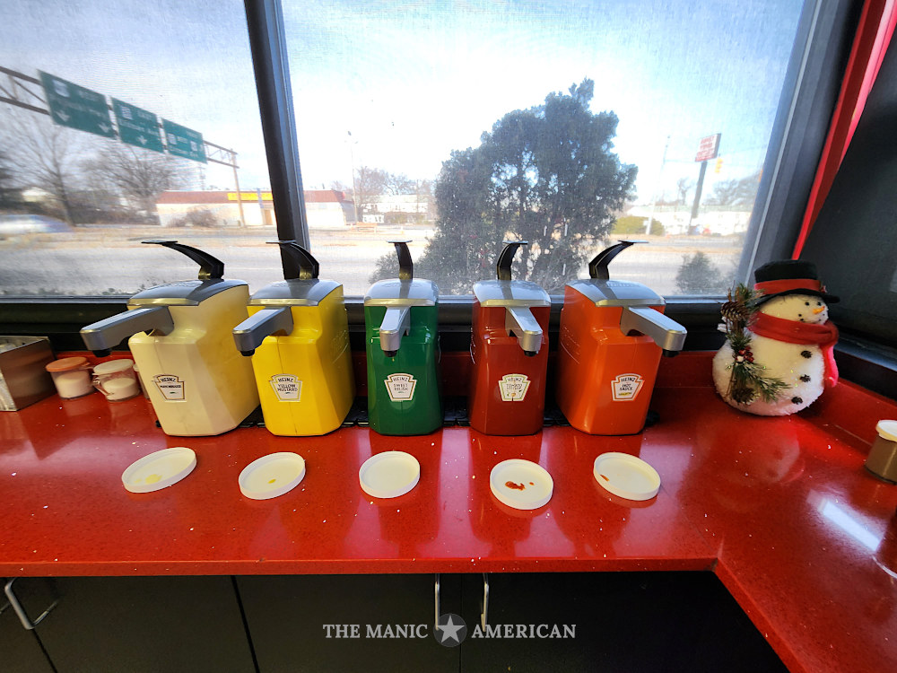 Colorful condiment dispensers sit next to a plush snowman inside a highwayside restaurant
